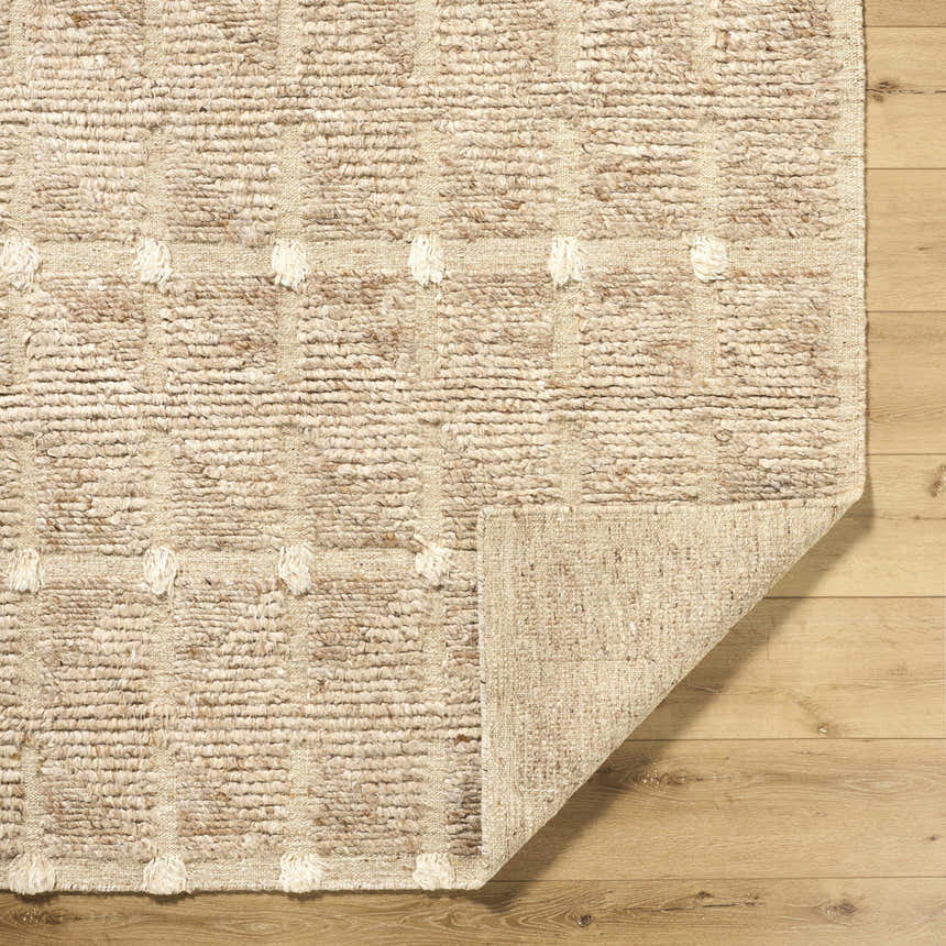 Close-up of the hand-woven Keegan Area Rug. Beige, sandstone, and taupe wool rug with a textured, dotted pattern. Fold
