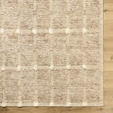 Close-up of the hand woven Keegan Area Rug. Beige, sandstone, and taupe wool rug with a textured, geometric pattern. Corner