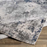 Close-up of Livabliss Aisha Surya AIS-2314 area rug. Abstract design in blue, charcoal, light gray, and off-white on wood floor. Fold