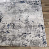 Close-up of Livabliss Aisha Surya AIS-2314 area rug. Abstract design in blue, charcoal, light gray, and off-white on wood floor. Front
