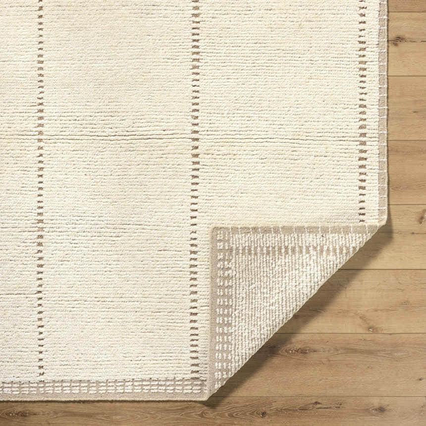 Close-up of the hand-knotted Kimani Area Rug. Ivory wool rug with sandstone dash pattern and a taupe geometric border. Fold