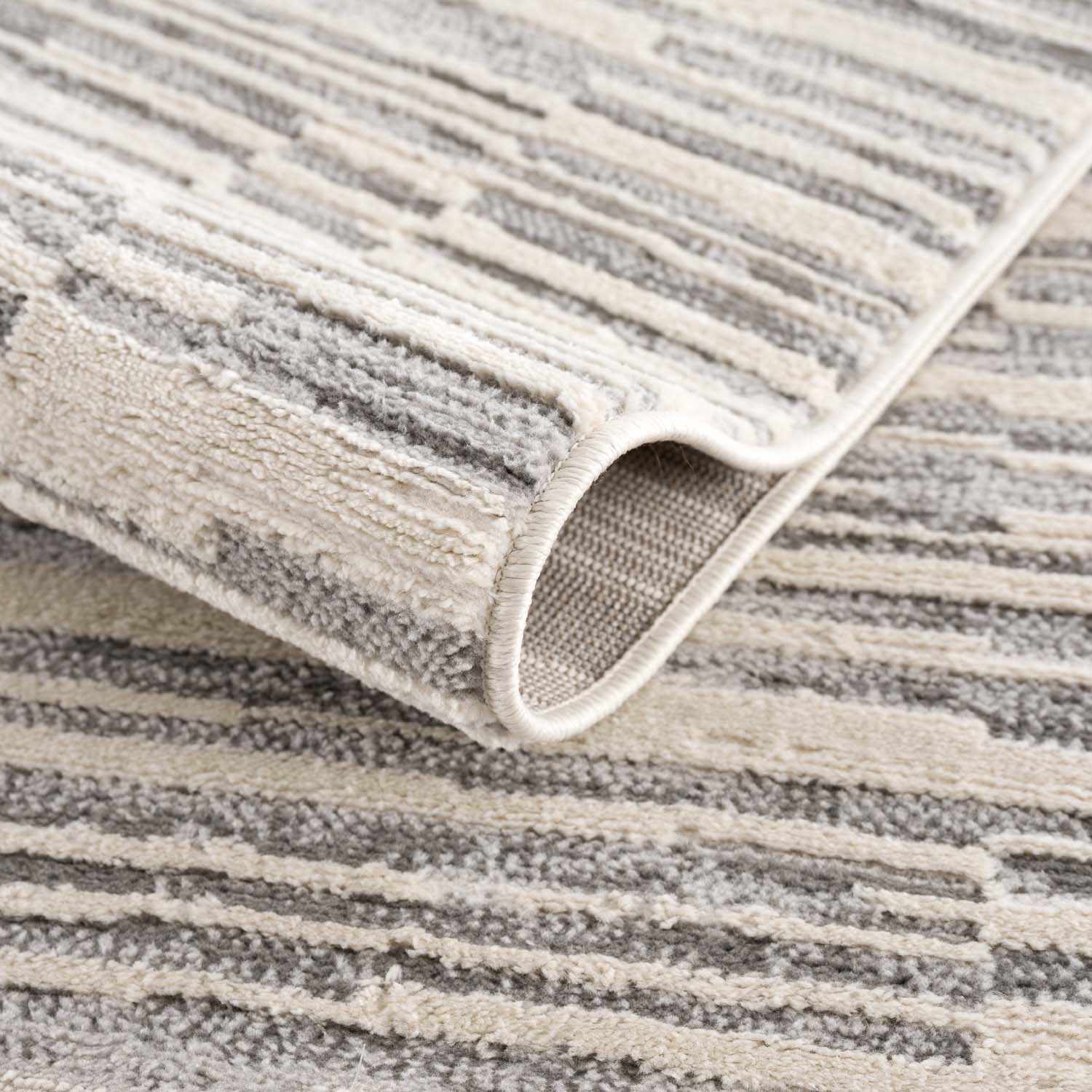 Folded section of Alexey Gray Broken-Striped Area Rug, displaying material thickness and weave. Contemporary Area Rug Backing  
