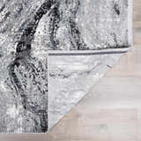 Close-up of the Littleport Luxury Fringed Faux Silk Rug. Abstract design in black, charcoal, gray, and light gray. Fold
