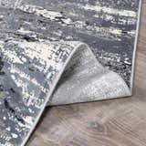 Close-up of Littleport Luxury Fringed Faux Silk Rug; abstract design in black, charcoal, gray, and light gray. Soft texture. Fold