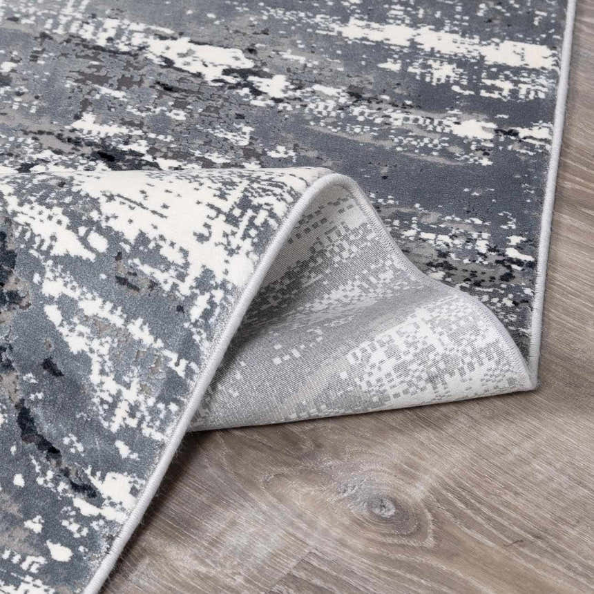 Close-up of Littleport Luxury Fringed Faux Silk Rug; abstract design in black, charcoal, gray, and light gray. Soft texture. Fold