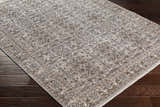Close-up of the Lugo Luxe Area Rug in light gray with traditional floral pattern and tassels on dark wood flooring. Corner