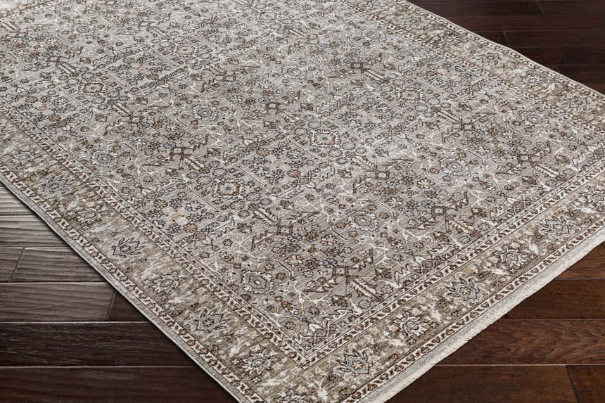 Close-up of the Lugo Luxe Area Rug in light gray with traditional floral pattern and tassels on dark wood flooring. Corner