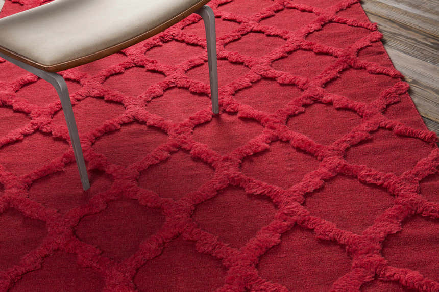 Close-up of the red Marilla Area Rug showing its shag texture and geometric trellis pattern, styled with a chair. Styleshot