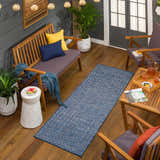 Outdoor patio scene with blue Maddingley Flatweave Area Carpet, wood furniture, string lights, and plants. Roomscene-Runner