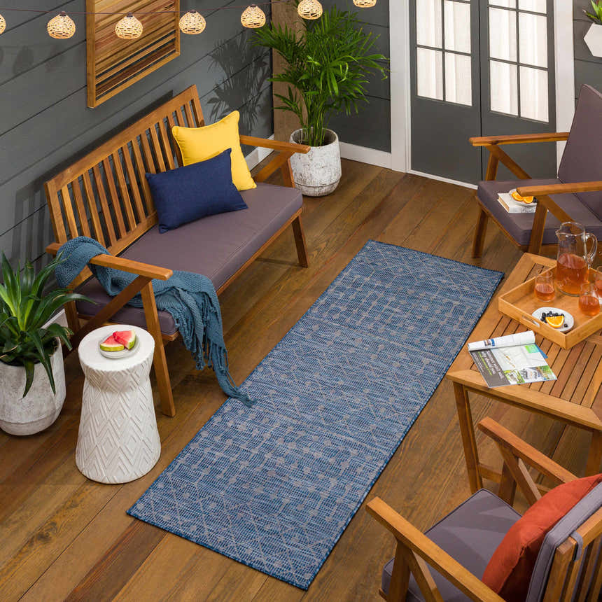 Outdoor patio scene with blue Maddingley Flatweave Area Carpet, wood furniture, string lights, and plants. Roomscene-Runner