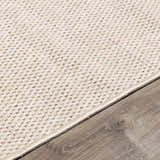 Close up of ivory Midha Area Rug showing woven texture and neutral border on wood floor. Corner