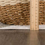 Close-up of Ulric Green Diamond Washable Area Rug pile height with a ruler and woven basket. Cream, green, and off-white colors. Pile