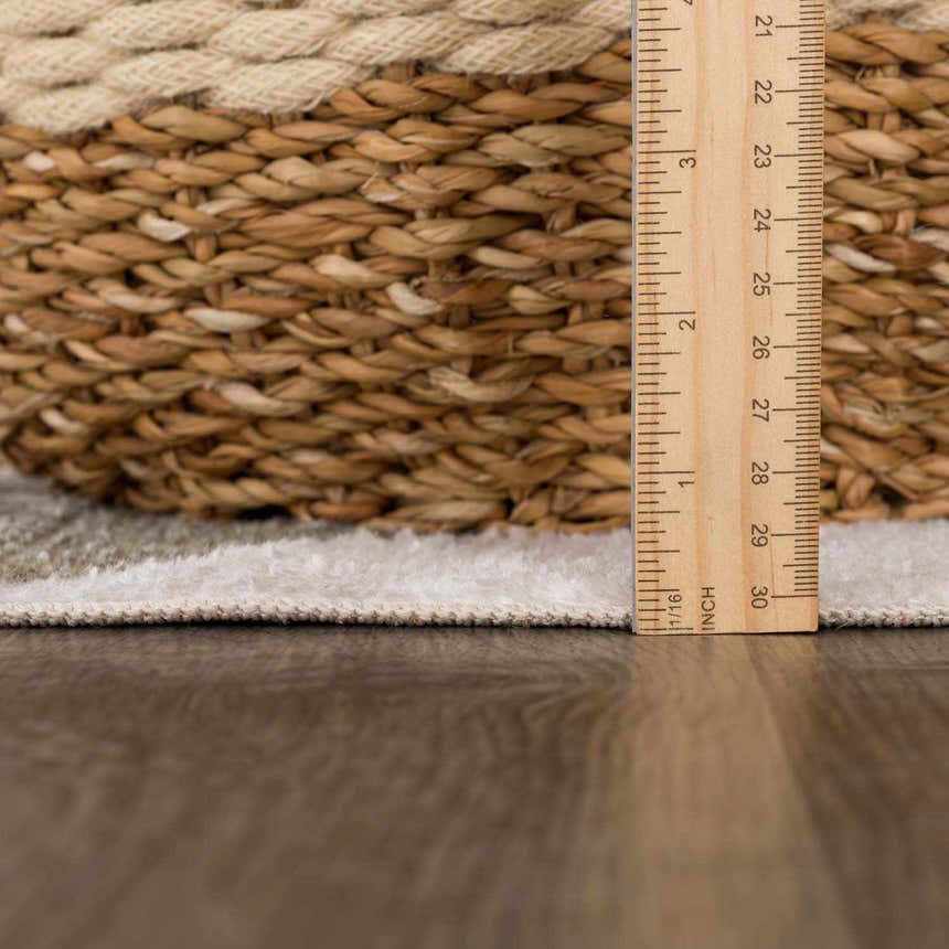 Close-up of Ulric Green Diamond Washable Area Rug pile height with a ruler and woven basket. Cream, green, and off-white colors. Pile