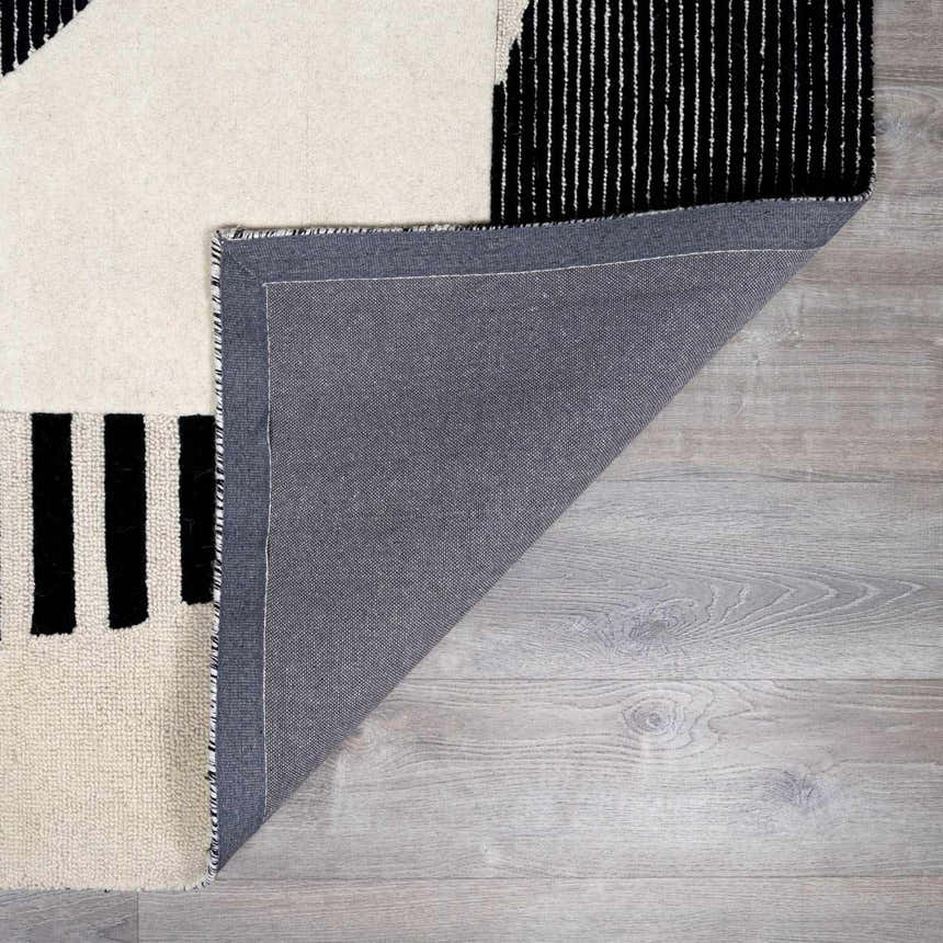 Close-up of the hand-tufted Brooklyn Modern wool area rug, showing geometric black and cream design and rug backing. Fold