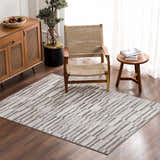 Living room scene with a gray and white Arissa Broken-Striped Area Rug, wood furniture, and a woven chair. Roomscene-Rectangle