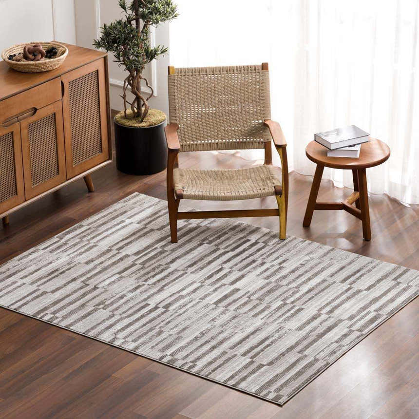 Living room scene with a gray and white Arissa Broken-Striped Area Rug, wood furniture, and a woven chair. Roomscene-Rectangle
