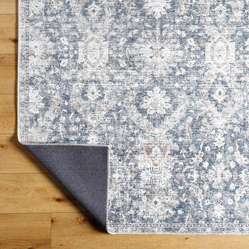 Close-up of the Arnaud Washable Area Rug, showcasing its beige, navy, and brown traditional floral pattern and texture. Fold