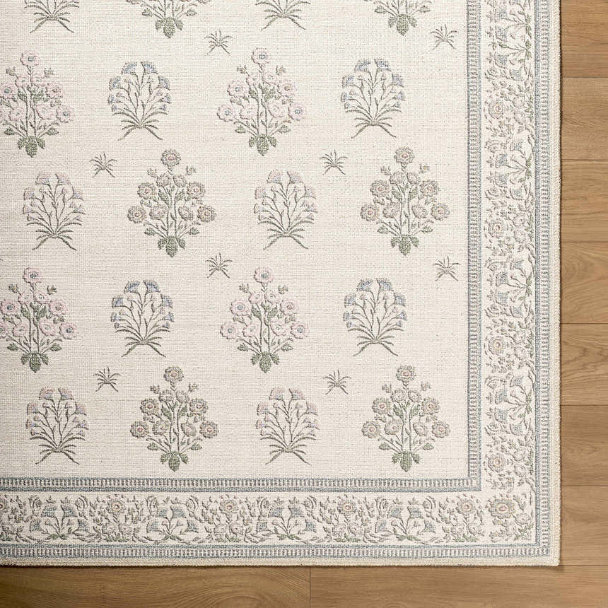 Close-up of Aquene Ivory Washable Area Rug. Features floral pattern in blush, sage, and sky blue with a decorative border. Corner