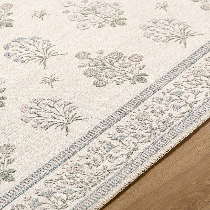 Close-up of the Aquene Ivory Washable Area Rug, showing a floral pattern in blush, sage, and sky blue on an ivory background. Texture