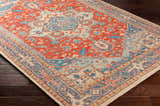 Close-up of the Oracabessa Premium Area Rug. Hand-knotted wool rug in blue, brick red, coral, and beige with a Persian-inspired design. Corner