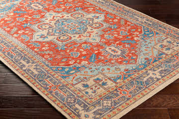 Close-up of the Oracabessa Premium Area Rug. Hand-knotted wool rug in blue, brick red, coral, and beige with a Persian-inspired design. Corner