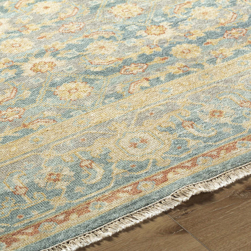 Close-up of the Papakura Area Rug showing its brick red, gray, mustard, and seafoam traditional floral pattern and fringe. Pile