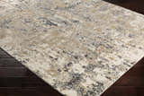 Close-up of the Pewamo Area Rug, a contemporary rug with black, charcoal, beige, and tan abstract pattern on dark wood floors. Corner