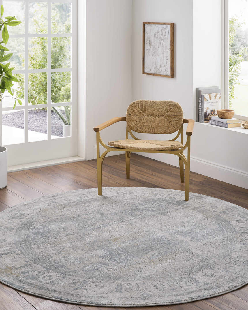 Sunlit room scene with a round Pryce Blue Gray rug, woven chair, and wood floors. Serene and stylish. Roomscene-Round