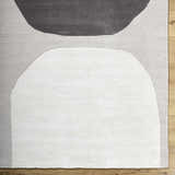 Close-up of the Adhara Area Rug, a hand-tufted wool rug with dark purple, medium gray, and sterling gray abstract shapes. Corner