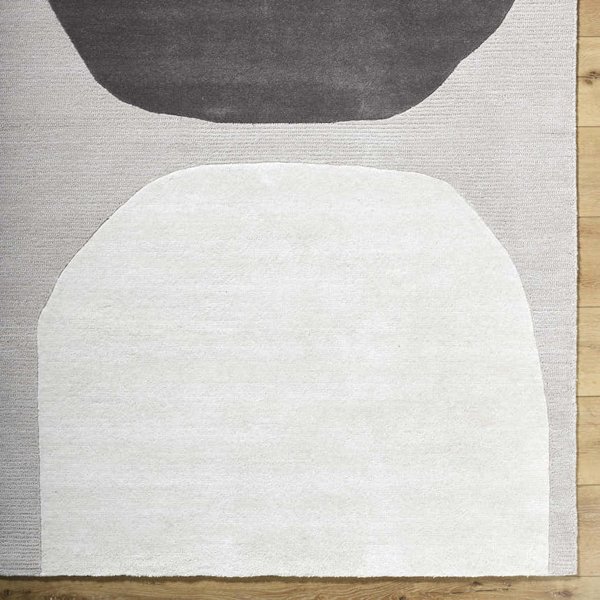 Close-up of the Adhara Area Rug, a hand-tufted wool rug with dark purple, medium gray, and sterling gray abstract shapes. Corner