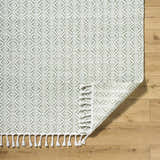 Close-up of the Anelia Sage Area Rug showing its green and ivory diamond pattern and braided fringe detail. Fold