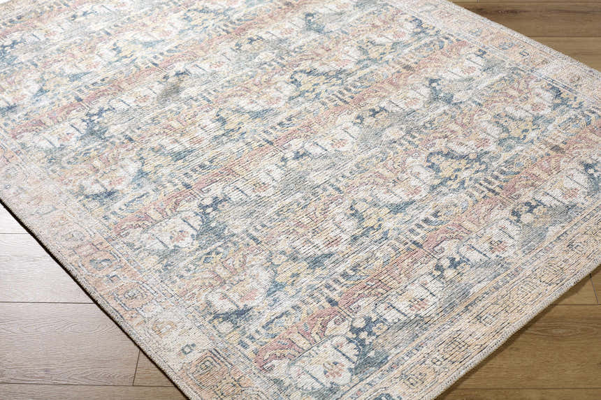 Close-up of the Arushi Washable Area Rug. Traditional design in cream, green, orange, rust, and tan. Machine woven texture. Corner