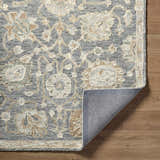 Close-up of Auryon Hand Tufted Oushak Wool Area Rug. Slate blue rug with off-white and tan floral pattern. Hand-tufted texture. Fold