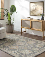 Living room scene with slate blue Auryon Hand Tufted Oushak Wool Area Rug, wood cabinet, potted plant, and neutral armchair. Roomscene-Rectangle