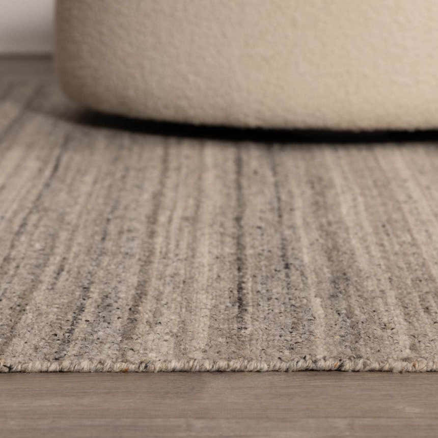 Close-up of the hand-tufted Capote Tan Area Rug showing its ash, charcoal, and taupe colors and textured wool design. Roomscene-Rectangle
