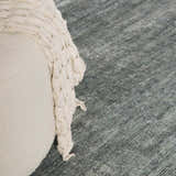 Close-up of the Livabliss x Galey Alix Maria Elena II rug in medium gray, with a cream pouf and knit throw blanket. Roomscene-Rectangle