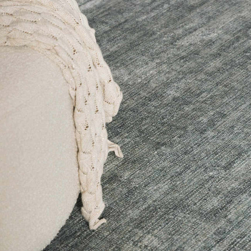 Close-up of the Livabliss x Galey Alix Maria Elena II rug in medium gray, with a cream pouf and knit throw blanket. Roomscene-Rectangle