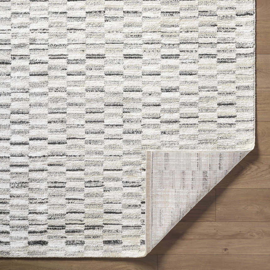Close-up of the Reece Luxe Rug showing its beige, black, and white contemporary block pattern and machine-woven texture. Fold