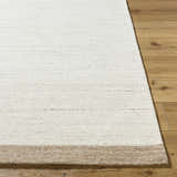 Close-up of the hand-tufted Amabel Area Rug showing its ivory, beige, and tan colors and wool texture on wood floor. Front