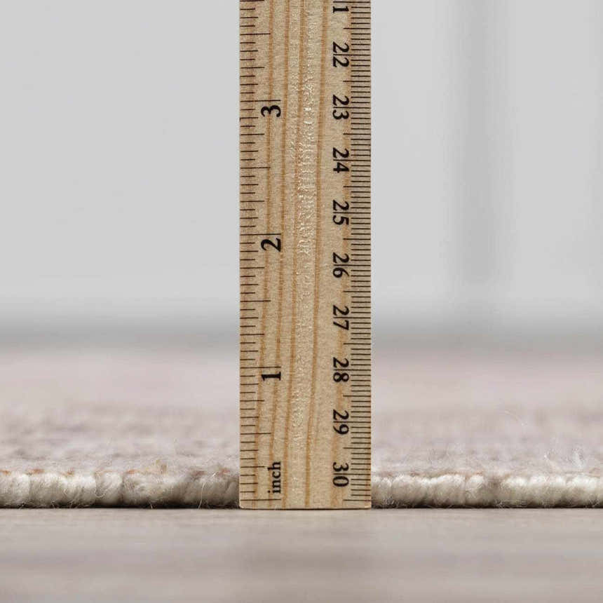 Close up of the Luciana III rug pile height with a ruler, showing beige and brown tones. Pile