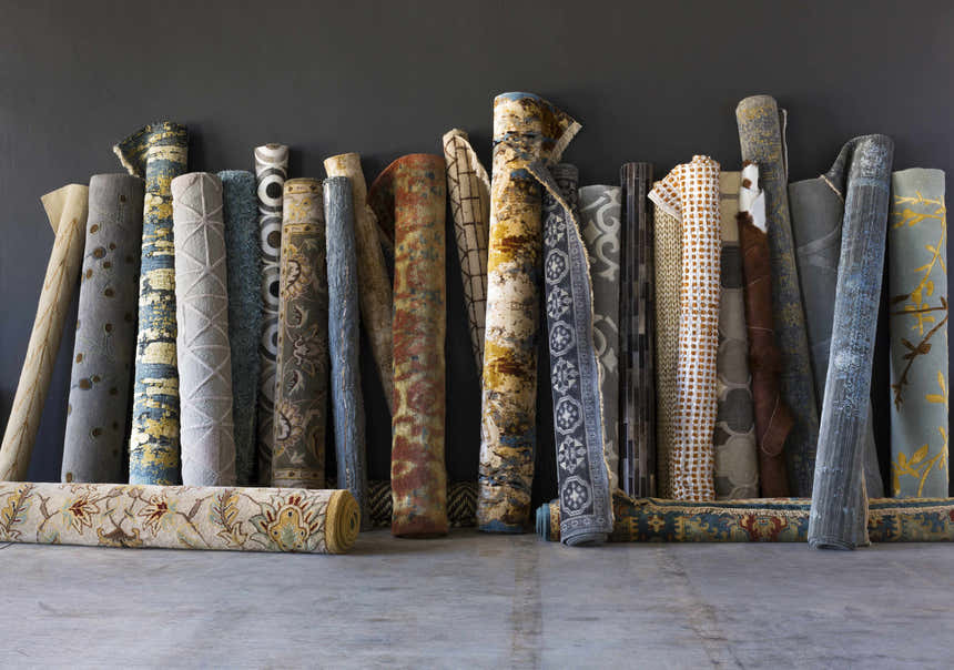 Rolled Sherwood Area Rugs in various colors and patterns against a dark gray wall. Rugs are on clearance. Styleshot