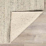 Close-up of the hand-woven Salvo Luxury Wool Area Rug showing its cream color, textured wool, and cotton backing. Fold