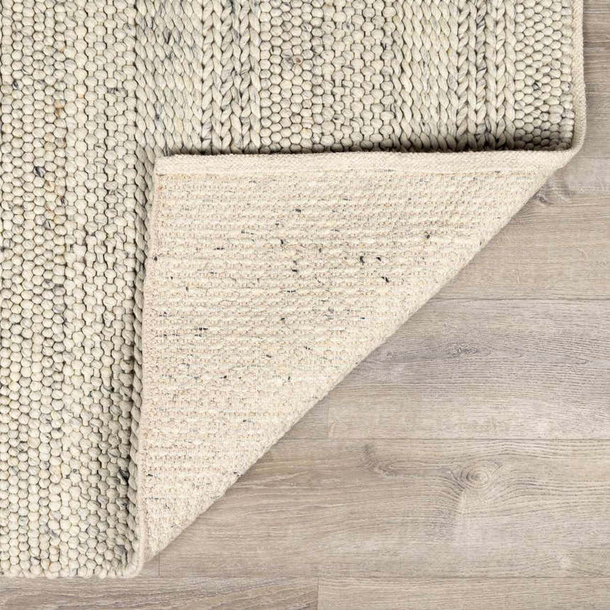 Close-up of the hand-woven Salvo Luxury Wool Area Rug showing its cream color, textured wool, and cotton backing. Fold