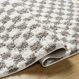 Close-up of the plush Kieu Taupe Checkered Rug, showing its gray and white checkered pattern and soft, textured pile. Fold