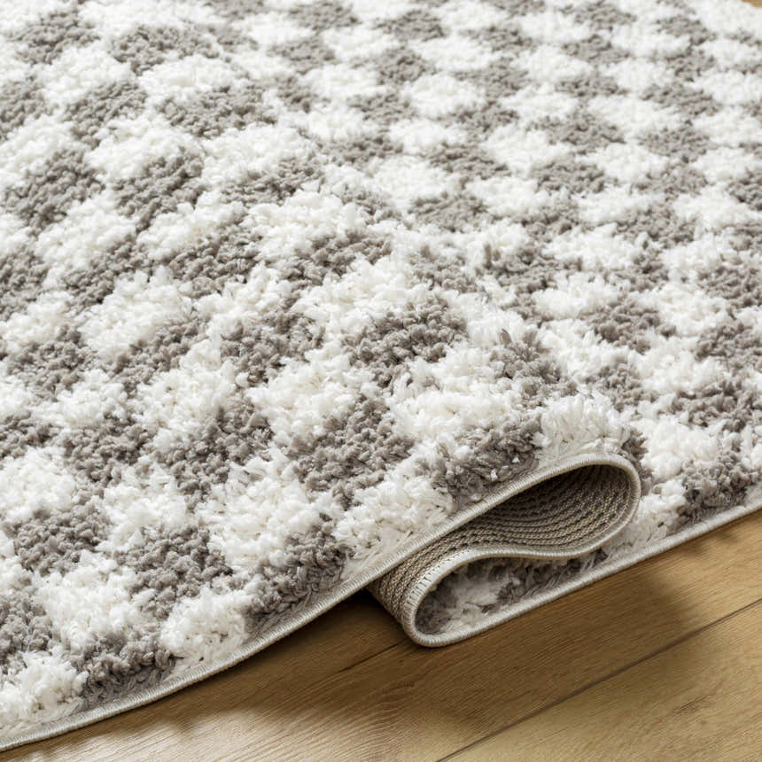 Close-up of the plush Kieu Taupe Checkered Rug, showing its gray and white checkered pattern and soft, textured pile. Fold