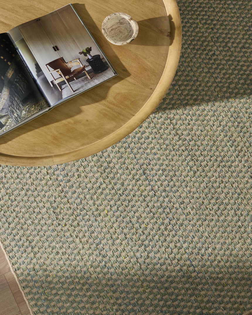Close-up of Verdel Sage rug showing sage, tan, and teal woven texture next to a wooden table with decor. Styleshot