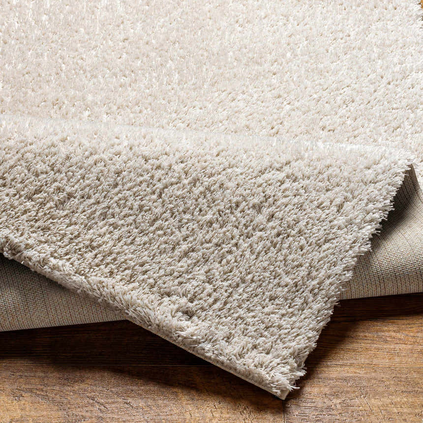 Close-up of the Livabliss Cloudy Shag CDG-2307 rug. The off-white polyester shag texture is visible. Fold