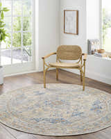 Bright room scene with a round Bora Area Rug in camel, copper, and blue under a woven chair. Roomscene-Round
