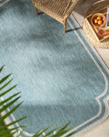 Outdoor patio scene with a light blue Arnola rug, wicker chair, and side table with fruit. Roomscene-Rectangle