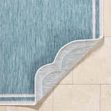 Close-up of the Arnola Light Blue Outdoor Rug showing its aqua color, woven texture, cream border, and backing. Fold